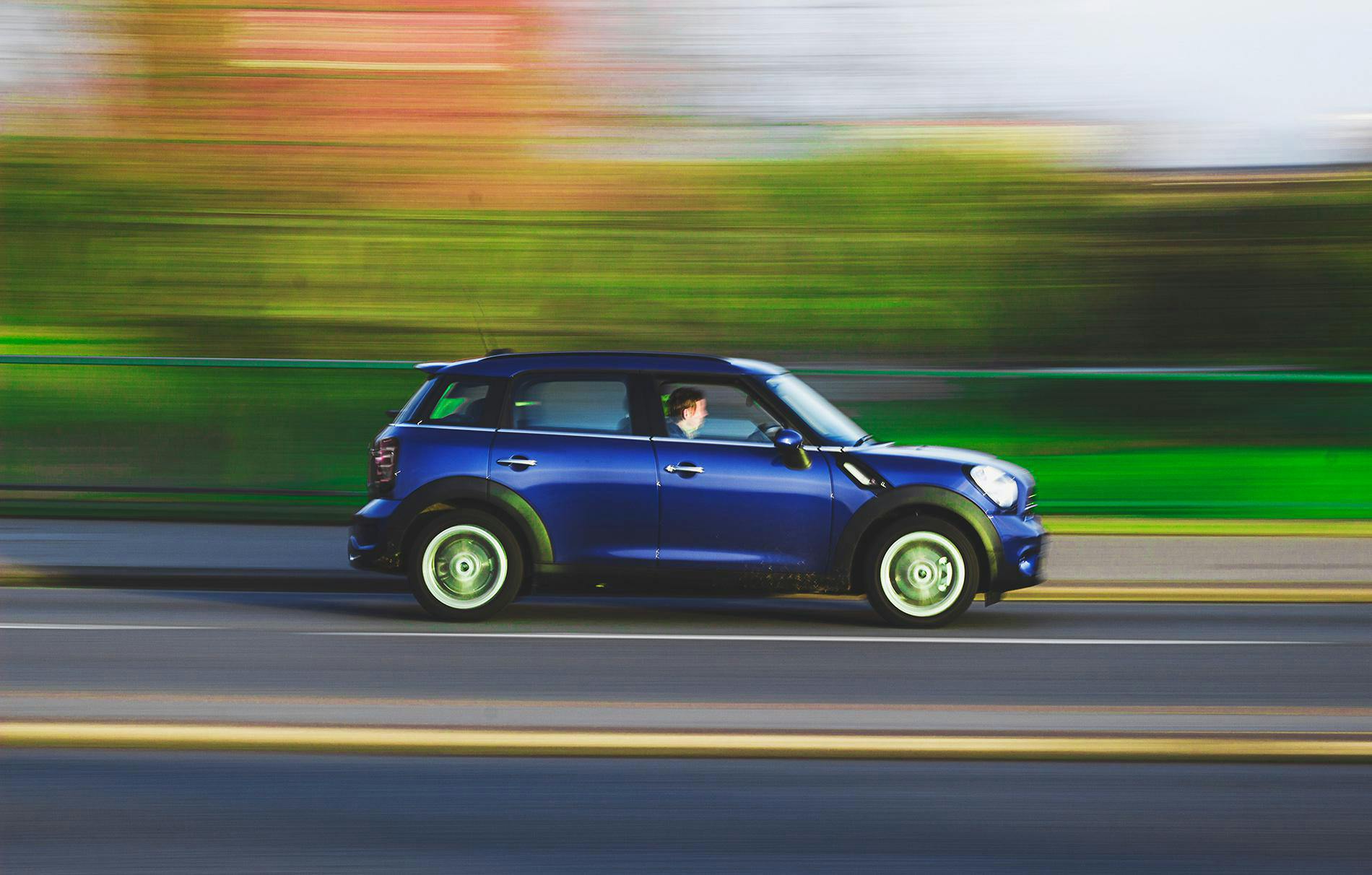 A blue car swiftly drives on a road with a blurred background, capturing speed and movement.
