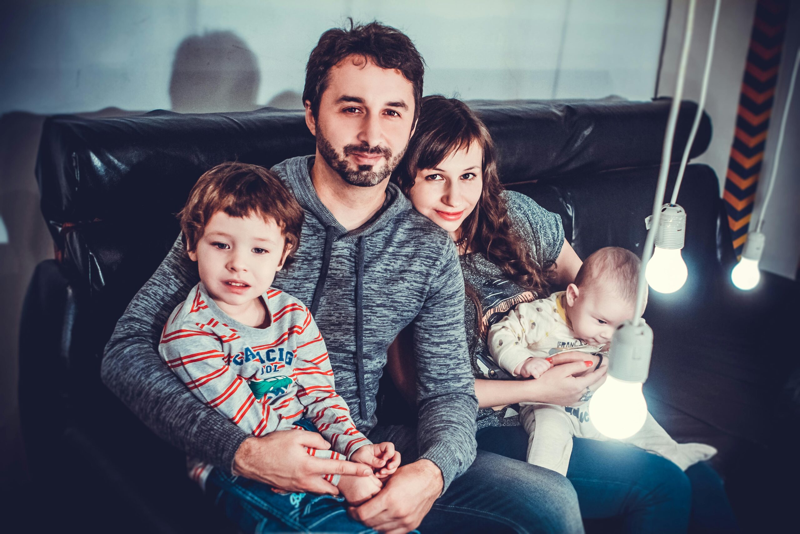 A joyful family of four sitting on a sofa, smiling warmly indoors.